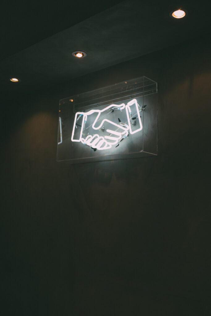 The commercial real estate deal agreement with the client is indicated by hand-shaking signs made of 3D lights.